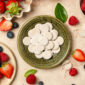 Comprimés de vitamine C UNAE dans un bol, entourés de fruits rouges (fraises, framboises, myrtilles) sur fond clair