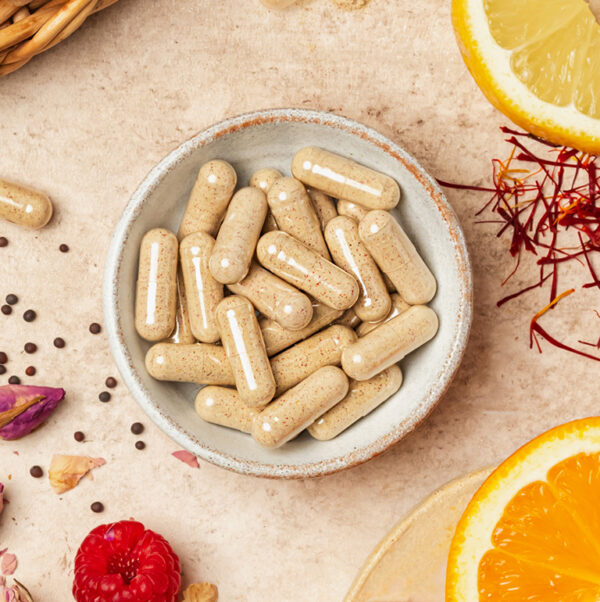 gelule_menopause Gélules complément ménopause UNAE dans un bol avec agrumes, framboise et safran sur fond clair